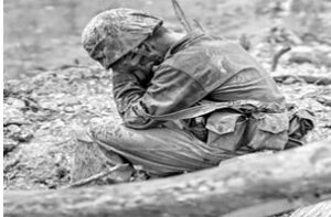 A soldier sitting on the ground looking sad